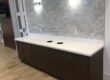 White countertop, dark cabinets, marble tile backsplash